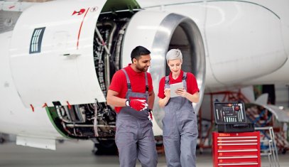 A man and a woman wearing overalls in front of a plane propeller
