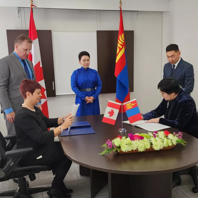 Officials sign agreement at table with Canadian and Mongolian flags in background