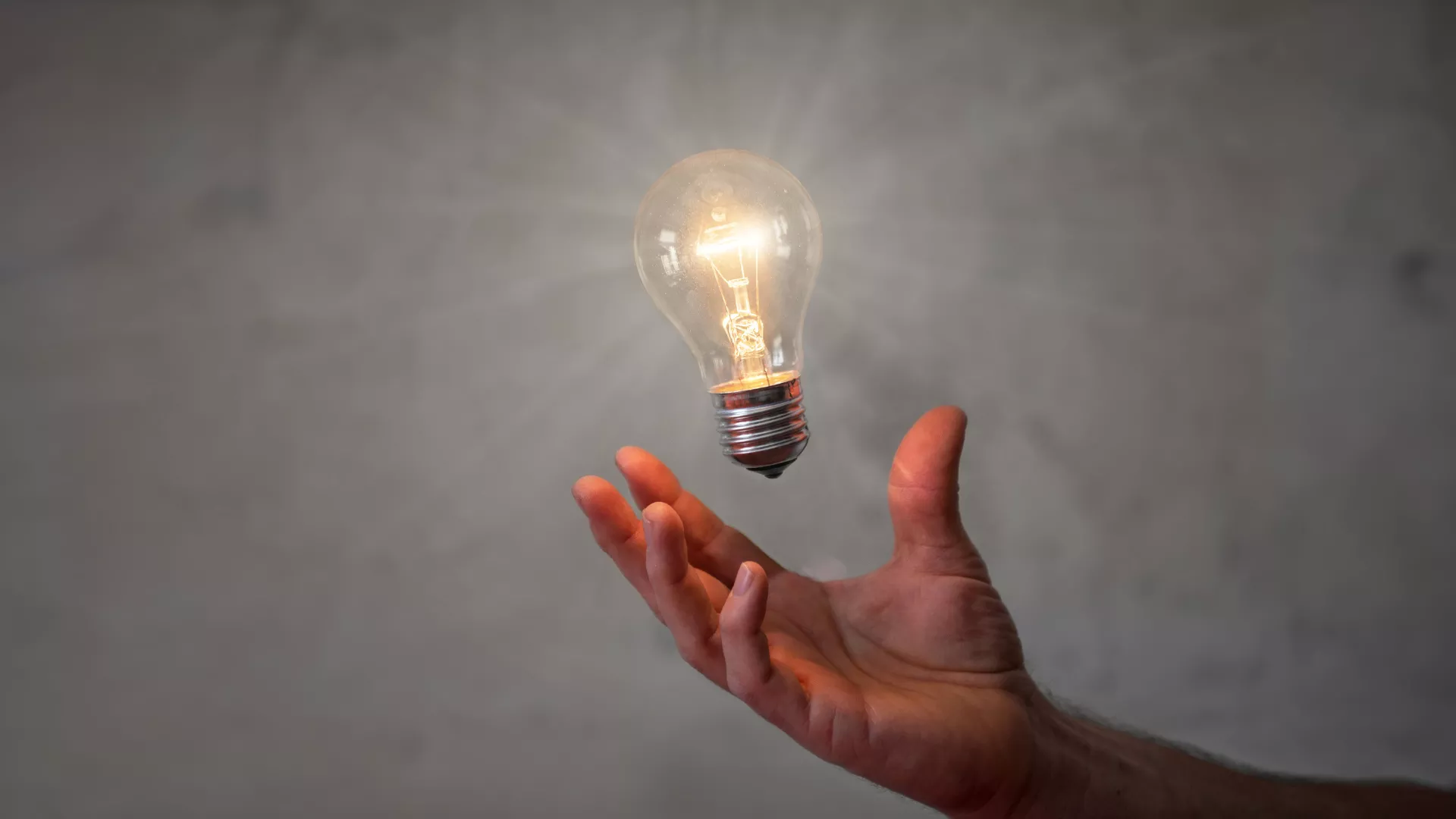 Hand holding lightbulb on grey background