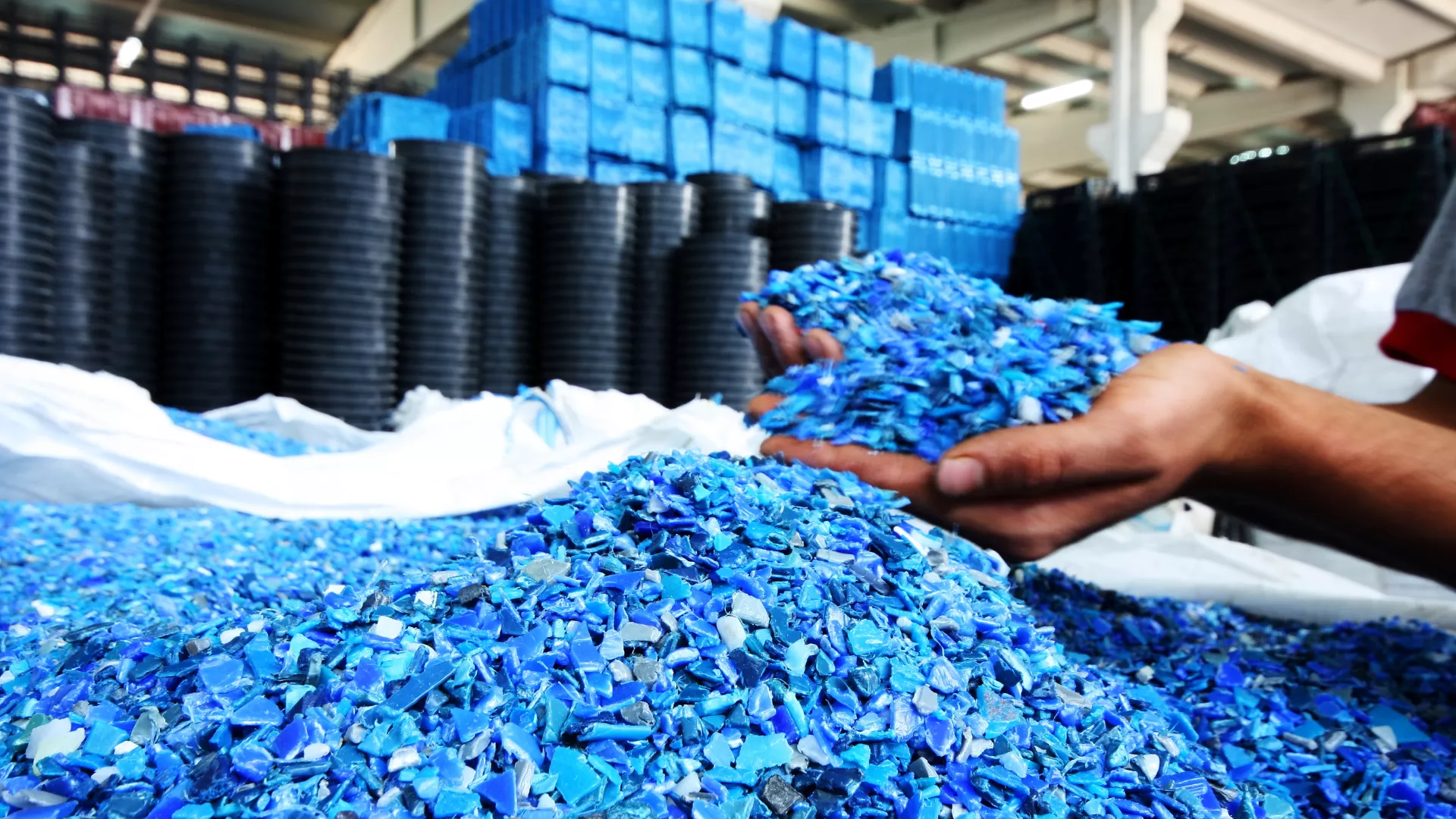 Someone digging their hands into a pile of recycled plastics that are the colour blue